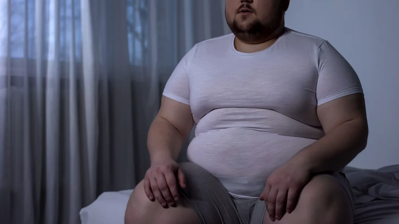 A man sitting on the edge of his bed, thinking
