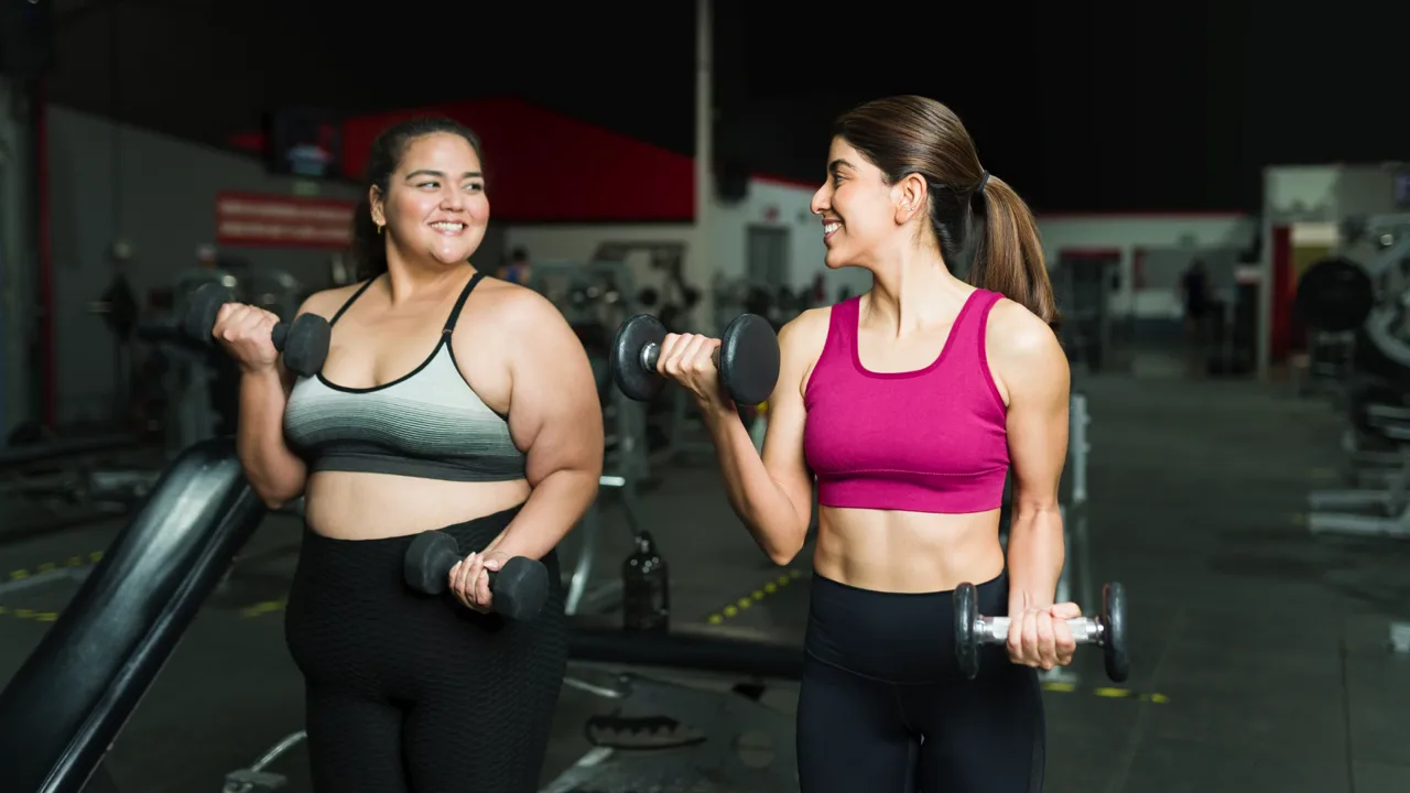 Two women lifting dumbbells together at the gym