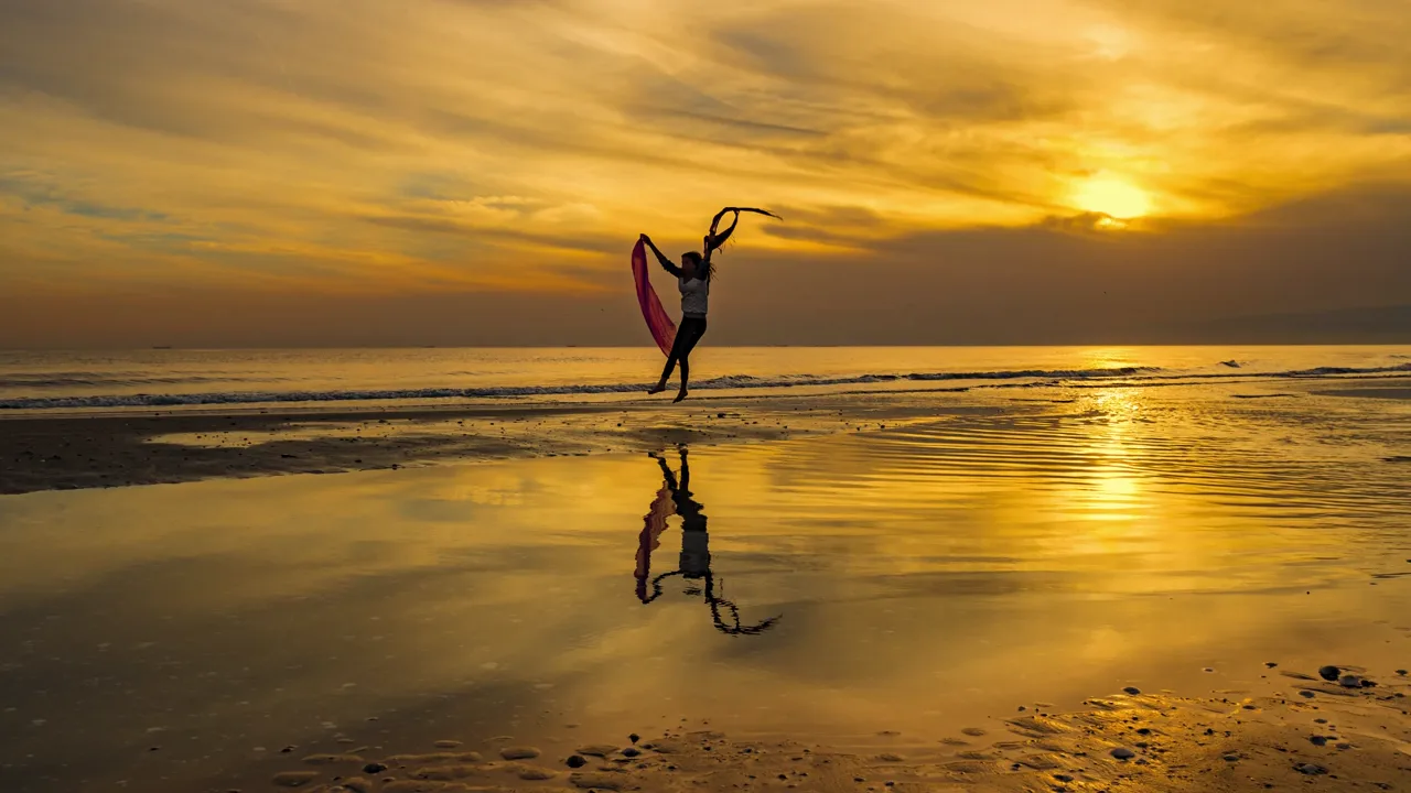 A woman stretching on a beach at sunset